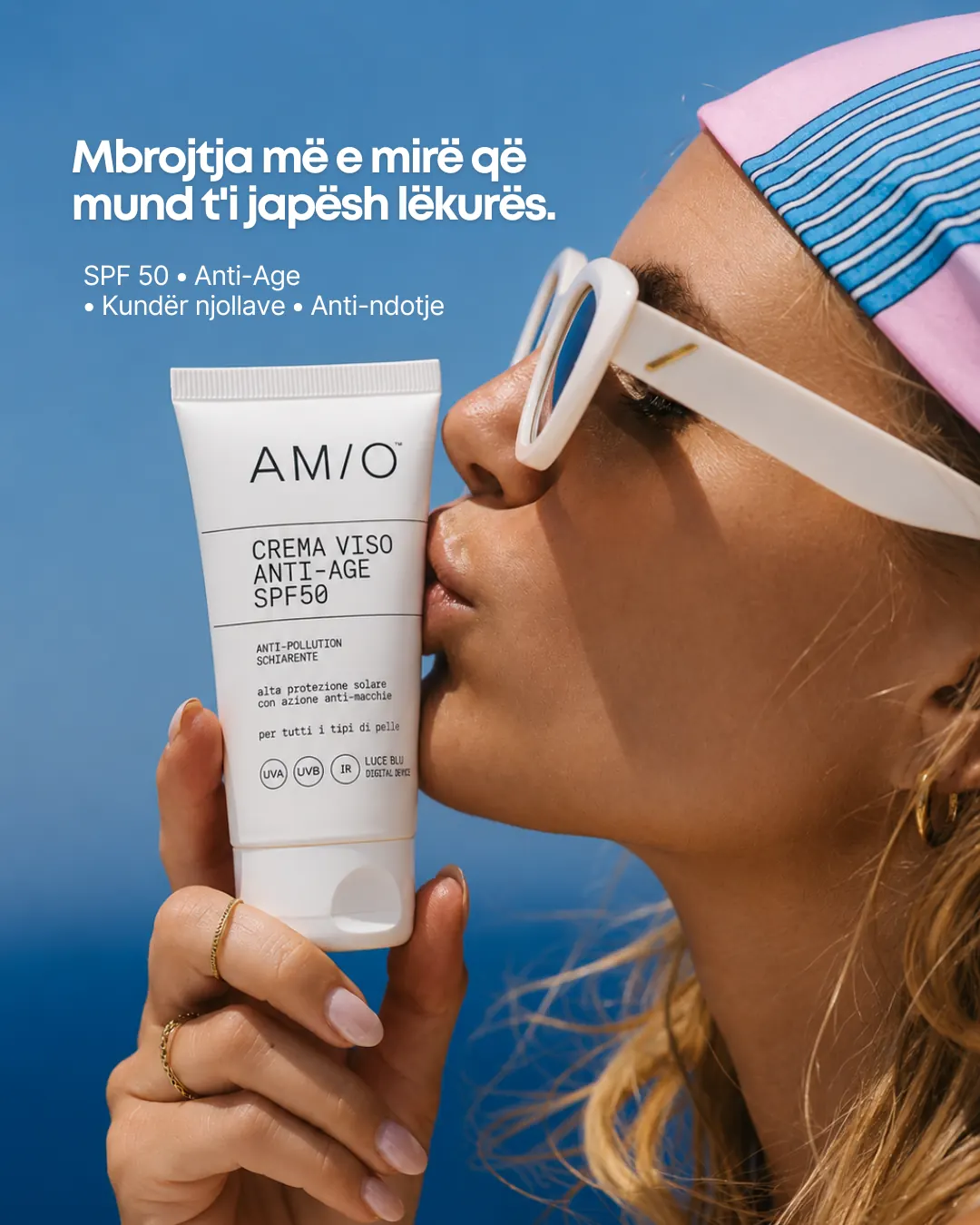 Am/o SPF 50 campaign frame — a model holding the Crema Viso Anti-Age SPF50 tube to her lips against a deep blue backdrop.